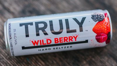 Truly wild berry hard seltzer can laying faceup on wooden surface.