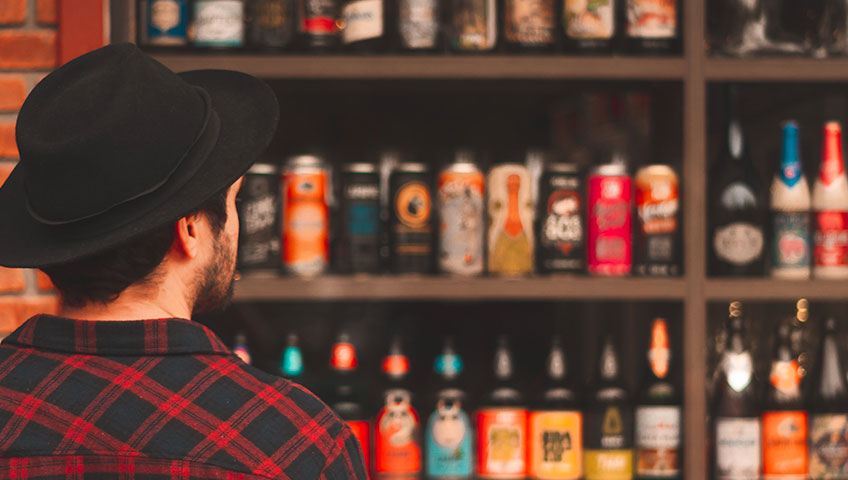 Male consumer staring at several shelves full of craft beer options and observing label design.