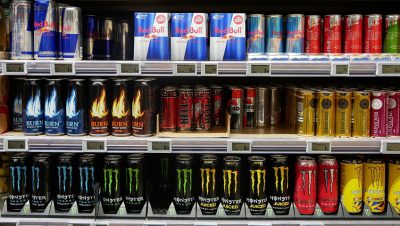 Three shelves in a supermarket full of various energy drink products displaying labels that meet legal requirements.