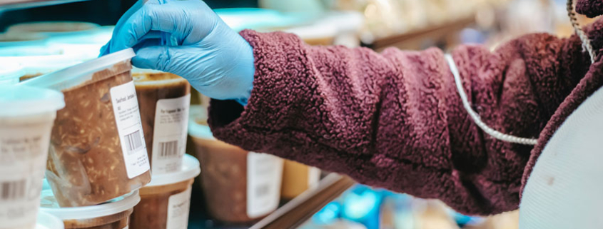 Female consumer wearing gloves and mask, inspecting labeled food packages during COVID pandemic.