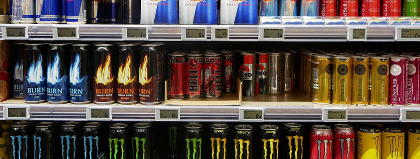 Three shelves in a supermarket full of various energy drink products displaying labels that meet legal requirements.