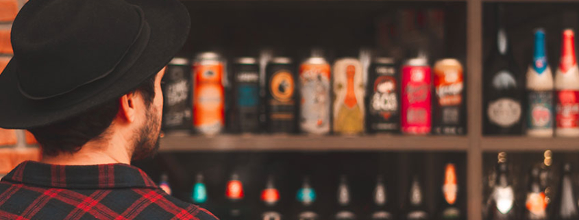 Male consumer staring at several shelves full of craft beer options and observing label design.