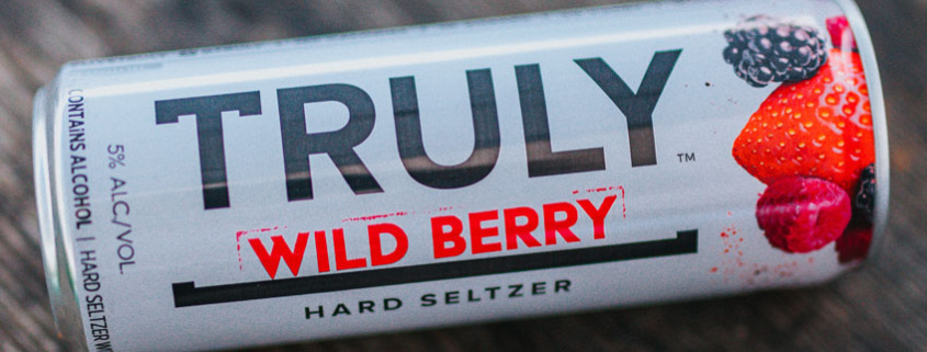 Truly wild berry hard seltzer can laying faceup on wooden surface.